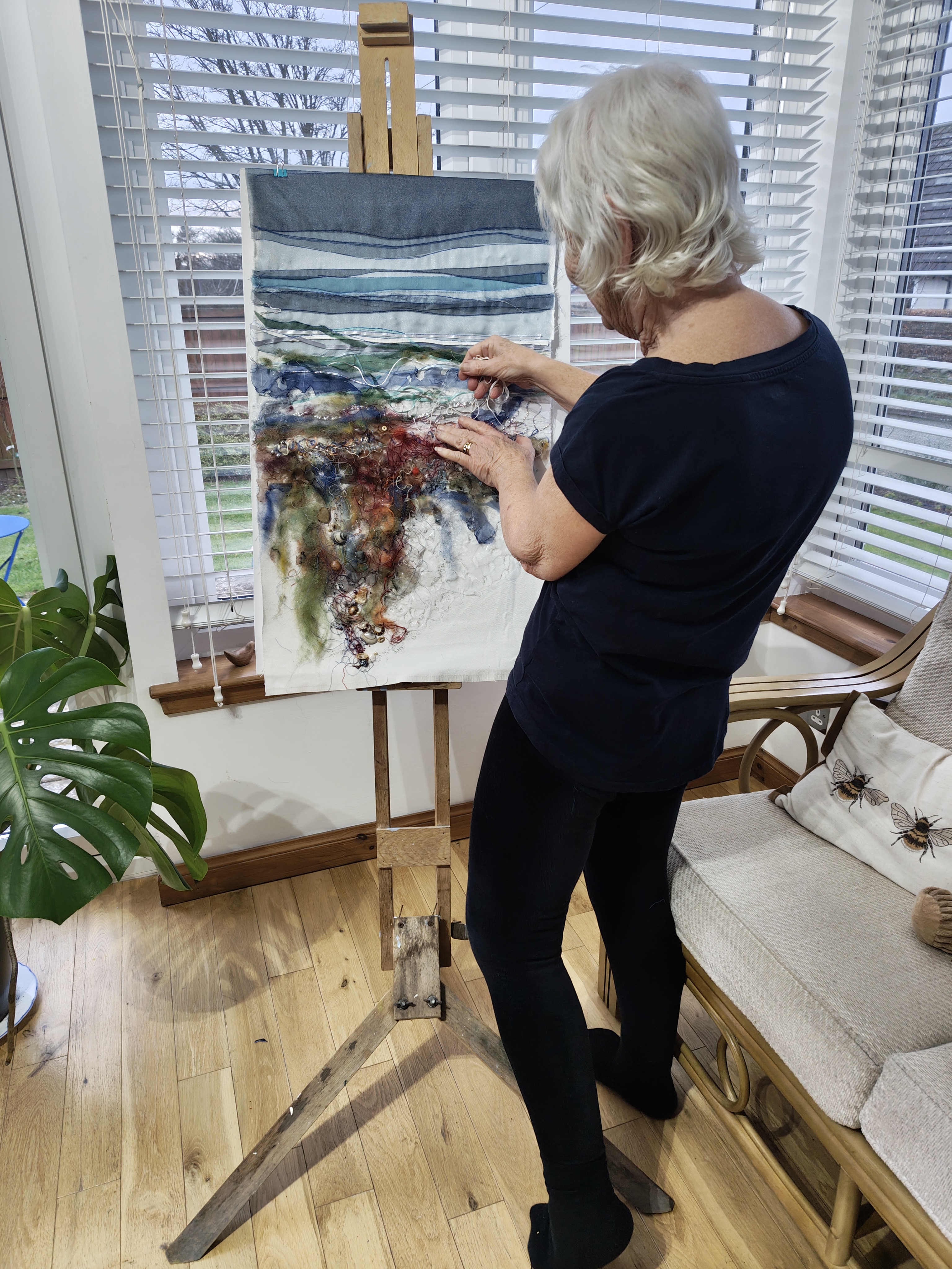 Artist at work on textile landscape on an easel.