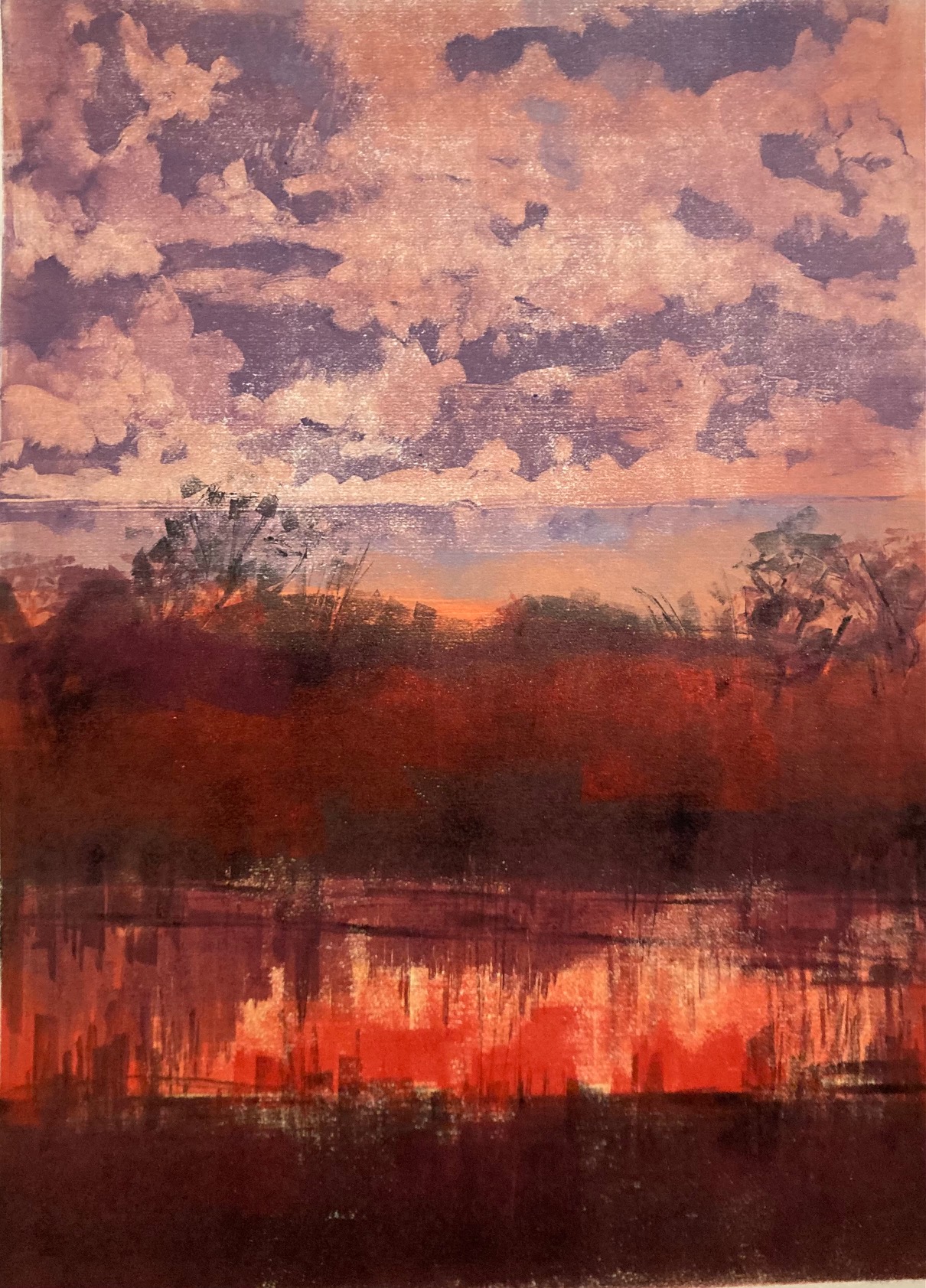 Dramatic early morning sunrise with hues of red, orange and yellow against a blue/grey cloudy sky with dark contrasting trees.